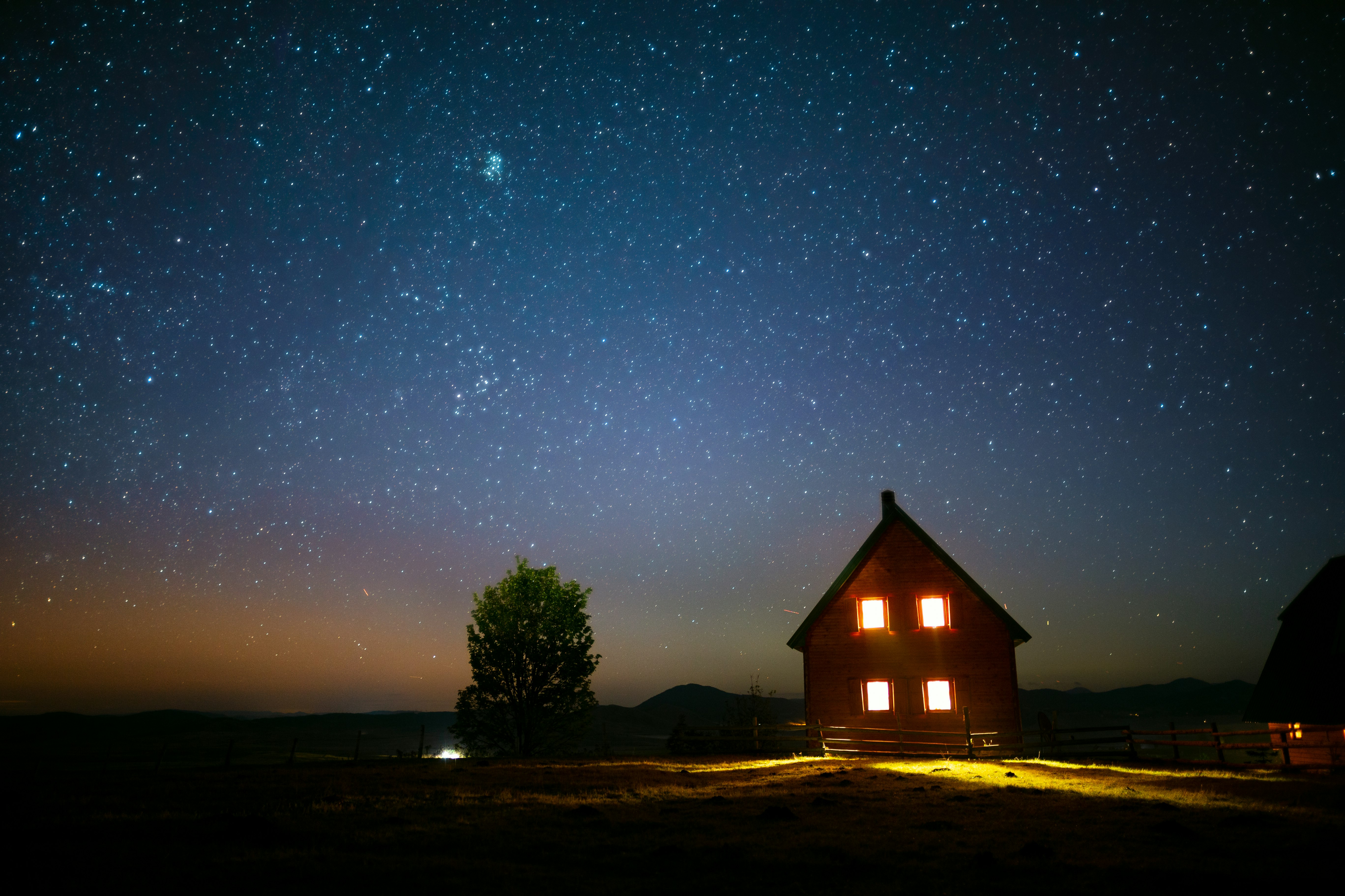 brown wooden house near green tree under blue sky during night time